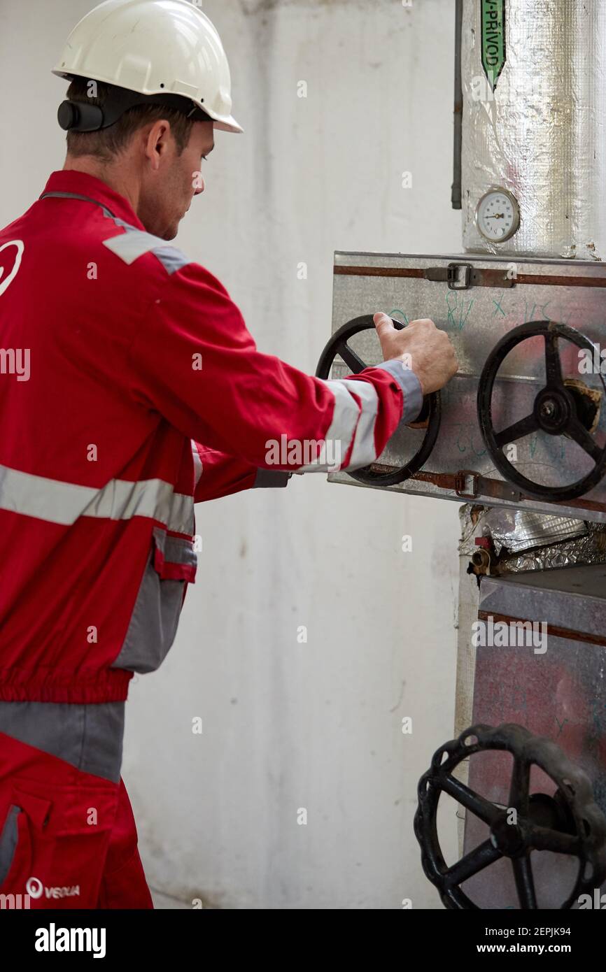 Industrie de l'énergie. Un technicien vêtu de combinaisons rouges et un casque blanc vérifiant les paramètres de chauffage. Technologie de distribution de l'eau de chauffage. Banque D'Images