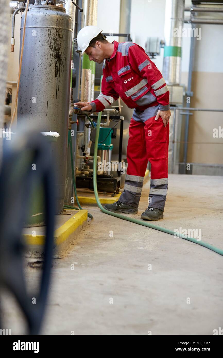 Industrie de l'énergie. Un technicien vêtu de combinaisons rouges et un casque blanc vérifiant les paramètres de chauffage. Technologie de distribution de l'eau de chauffage. Banque D'Images