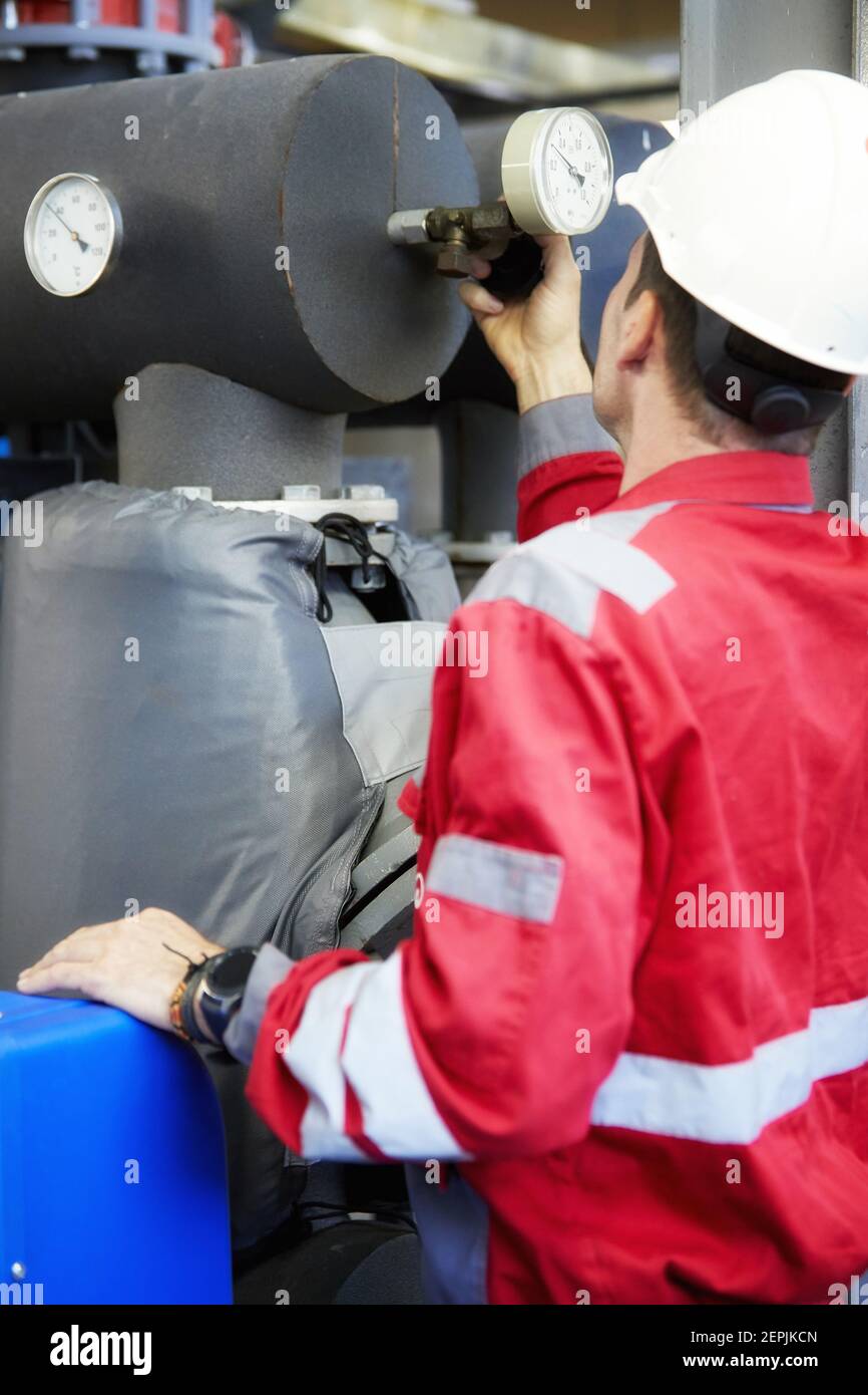 Industrie de l'énergie. Un technicien vêtu de combinaisons rouges et un casque blanc vérifiant les paramètres de chauffage. Technologie de distribution de l'eau de chauffage. Banque D'Images