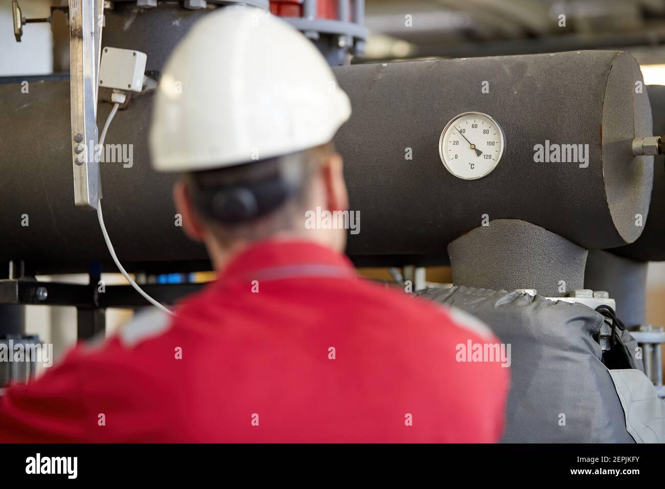 Industrie de l'énergie. Un technicien vêtu de combinaisons rouges et un casque blanc vérifiant les paramètres de chauffage. Technologie de distribution de l'eau de chauffage. Banque D'Images