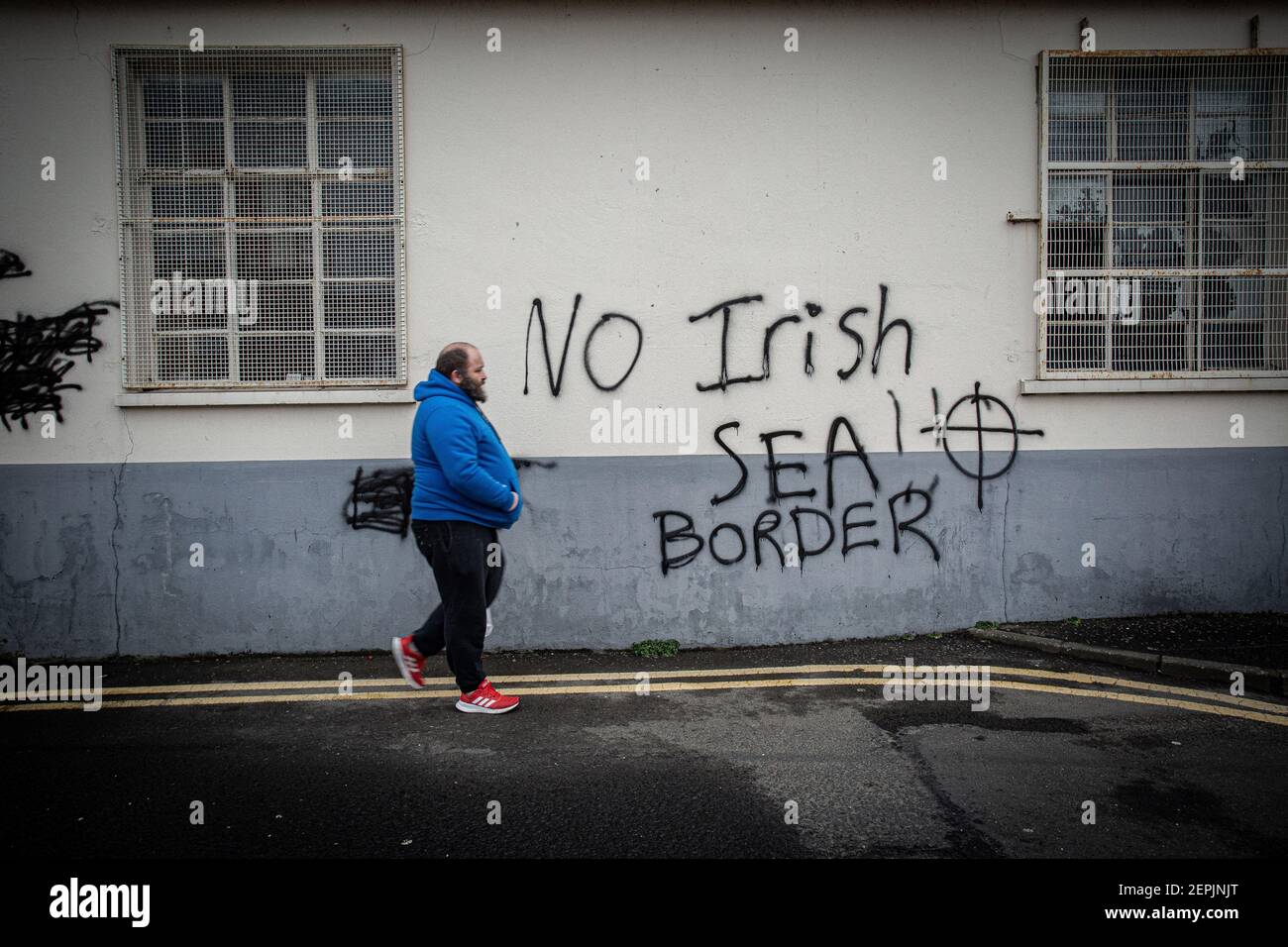 LARNE, IRLANDE DU NORD - février 24 : Un homme passe devant un graffiti loyaliste menaçant destiné au personnel portuaire de Larne, Irlande du Nord. Banque D'Images