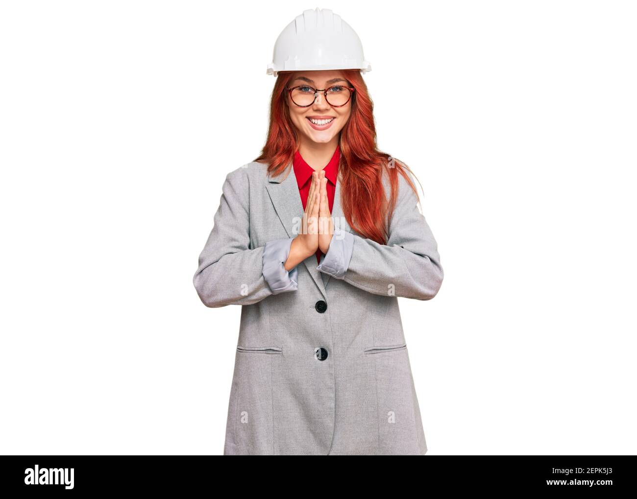 Jeune femme à tête rouge portant un chapeau d'architecte priant avec les mains ensemble demandant pardon souriant confiant. Banque D'Images