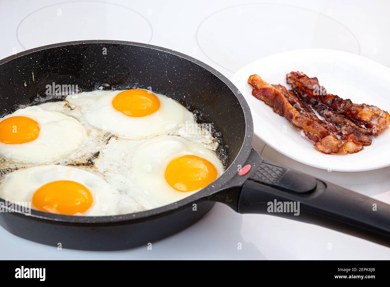 Un petit déjeuner nutritif composé d'œufs frits et de bacon croustillant. Le processus de cuisson d'un groupe d'œufs dans une casserole. Bacon croustillant sur une assiette. Idée pour un rapide, hea Banque D'Images