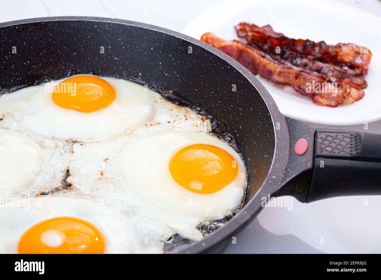 Un petit déjeuner nutritif composé d'œufs frits et de bacon croustillant. Le processus de cuisson d'un groupe d'œufs dans une casserole. Bacon croustillant sur une assiette. Idée pour un rapide, hea Banque D'Images