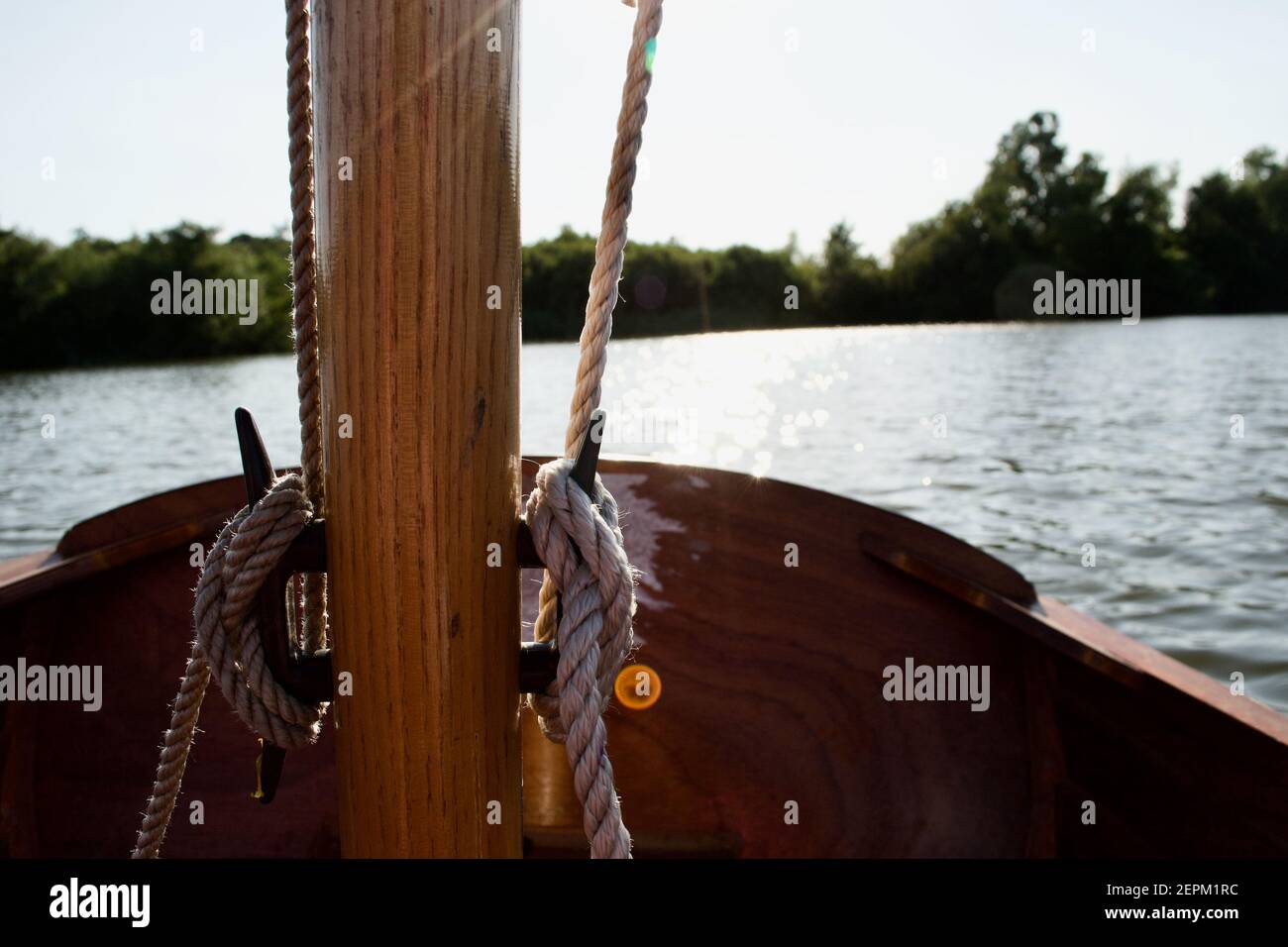 Gros plan des crampons sur le mât en bois d'un petit voilier (canot pneumatique) : cordes (halyards) attachées en nœuds libres, un lac ou une rivière en arrière-plan Banque D'Images