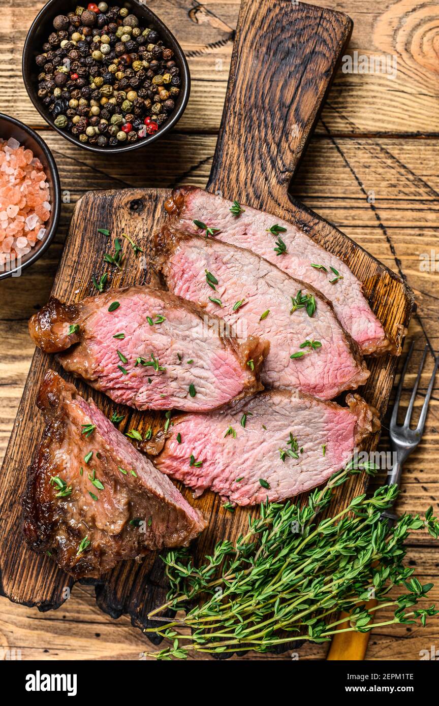Tranches rares de rôti de boeuf sirloin à trois pointes steak bbq sur une planche à découper en bois. fond en bois. Vue de dessus Banque D'Images