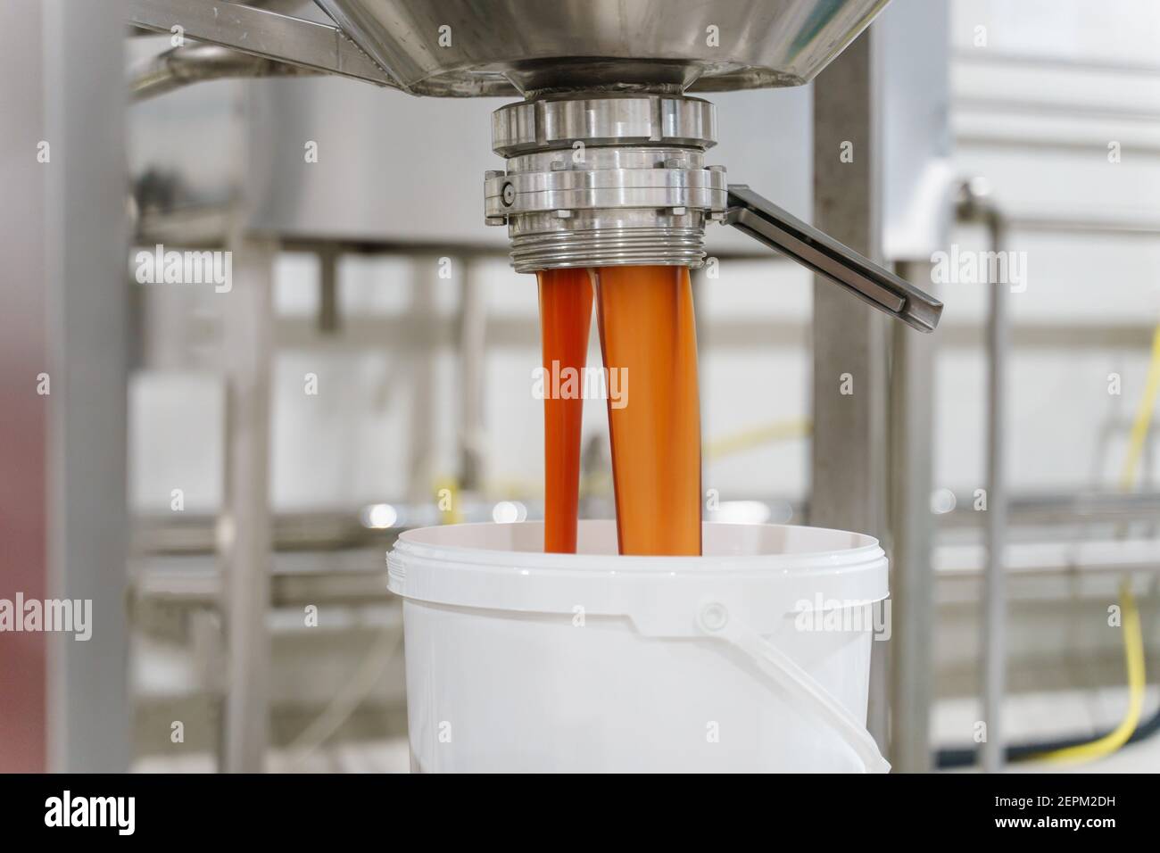 Gros plan sur la main d'un inconnu portant un gant de protection ouverture des silos avec de la crème ou de la marmelade lors du versement en usine dans l'ensemble seau - nourriture Banque D'Images