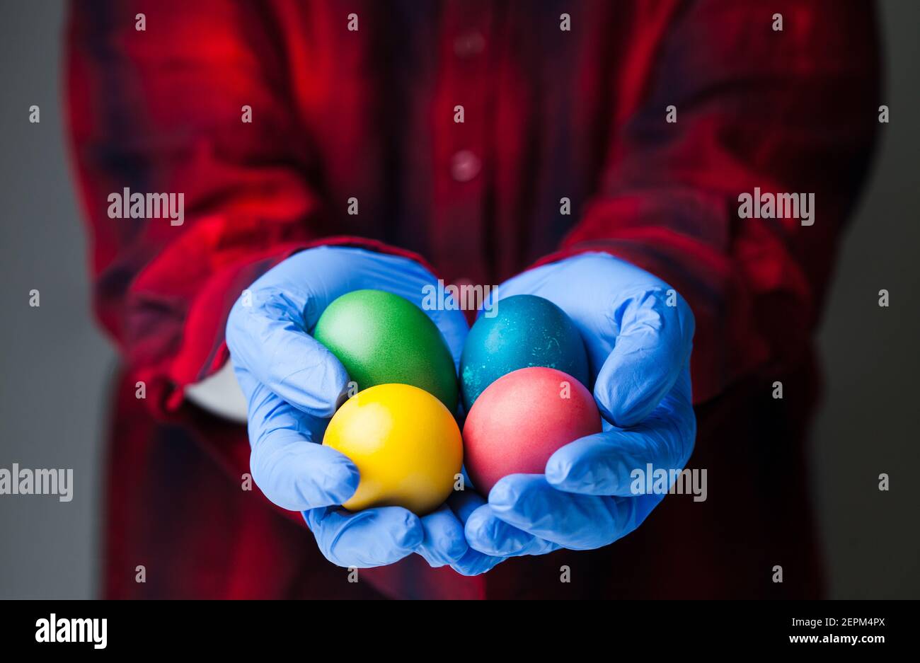 Personne portant des gants de protection médicale bleus tenant des œufs de Pâques de couleur, vacances dans le cadre de la pandémie mondiale du coronavirus COVID-19, dans le monde entier Banque D'Images