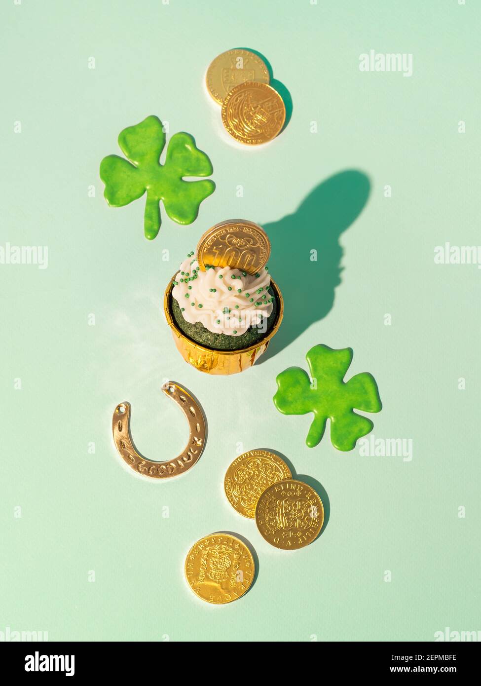 Concept de la St Patrick. Encore plus moderne avec des symboles chanceux et de la nourriture douce pour la fête de la Saint Patrick. Cupckake au velours vert, shamrock, pièces de monnaie dorées et fer à cheval sur fond vert. Verticale Banque D'Images