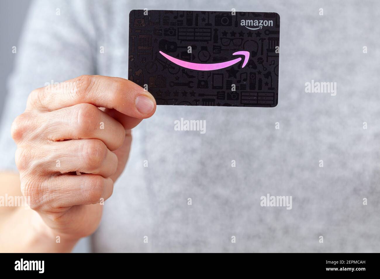 Clarksburg, Maryland, Etats-Unis 02-25-2021: Une femme caucasienne tient une carte-cadeau de Amazon.com (fond noir avec logo rose). Une idée de cadeau polyvalente populaire Banque D'Images