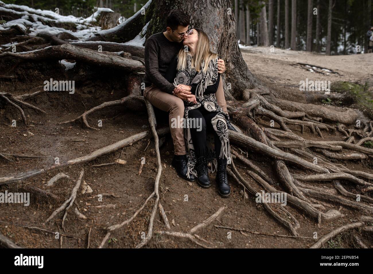 Corps complet de couple doux positif assis près de l'arbre et embrasser et s'embrasser pendant une journée romantique dans les bois Banque D'Images