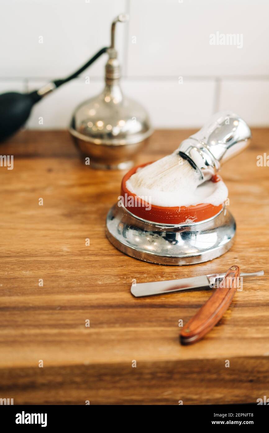 Par le dessus de la brosse de rasage avec poils doux dans le bol avec du savon moussant près du rasoir droit sur une table en bois Banque D'Images