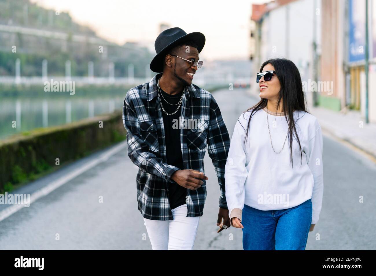 Les jeunes sont des partenaires multiraciaux dans des vêtements et des lunettes de soleil à la mode qui parlent tout en regardant les uns les autres et en se promenant sur la route de la ville Banque D'Images