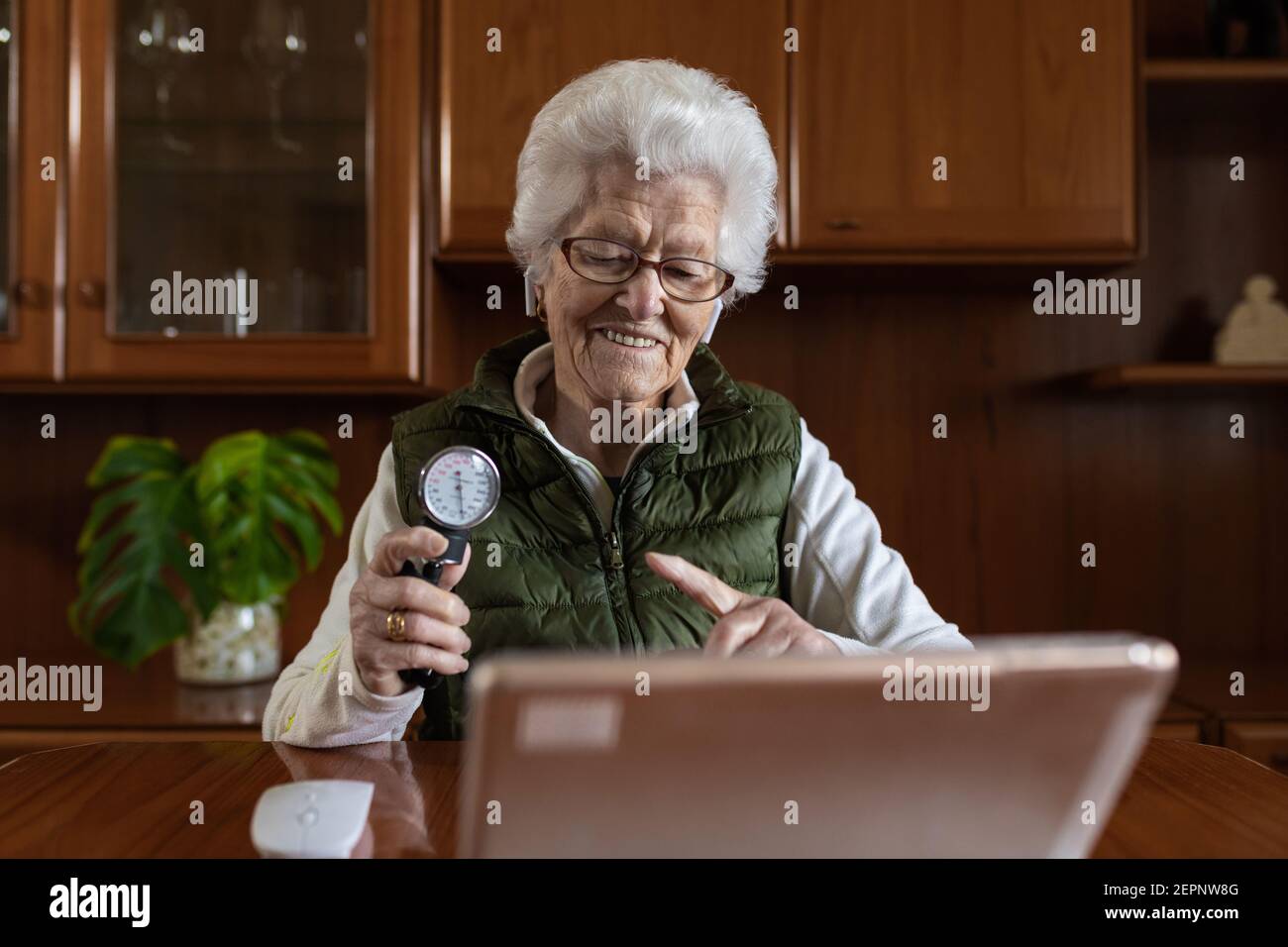 Femme âgée souriante et sénataire pointant vers le sphygmomanomètre tout en parlant chat vidéo contre tablette lors de la consultation en ligne sur la santé à la maison Banque D'Images