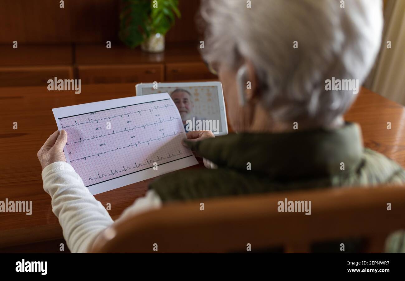 Vue arrière de la récolte anonyme femelle retraité avec électrocardiogramme sur papier contre tablette avec médecin à l'écran pendant la santé en ligne consultation à Banque D'Images