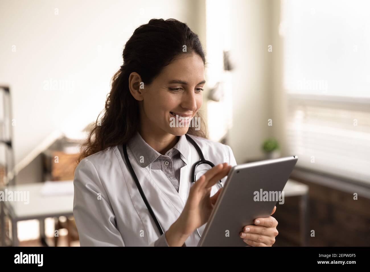 Une femme médecin souriante se tient debout au bureau avec une tablette Banque D'Images