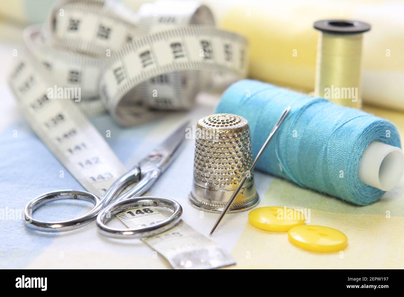 outils de couture avec ciseaux, fils, aiguille et mètre à ruban. Accessoires pour couturiers sur tissus bleus et jaunes Banque D'Images
