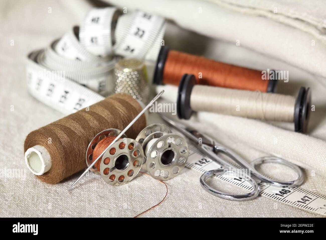 outils de couture avec ciseaux, fils bruns, aiguille et mètre ruban. Accessoires de couturiers sur tissus beige Banque D'Images