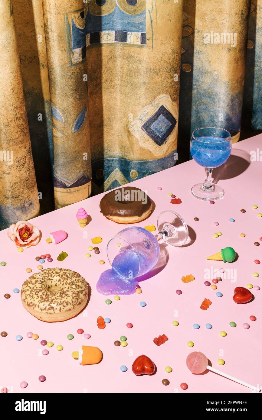 Concept minimaliste après la fête avec petite glace, boisson créative rose dans des verres à vin, bonbons et pop de lally sur le fond rose de la table et aller Banque D'Images