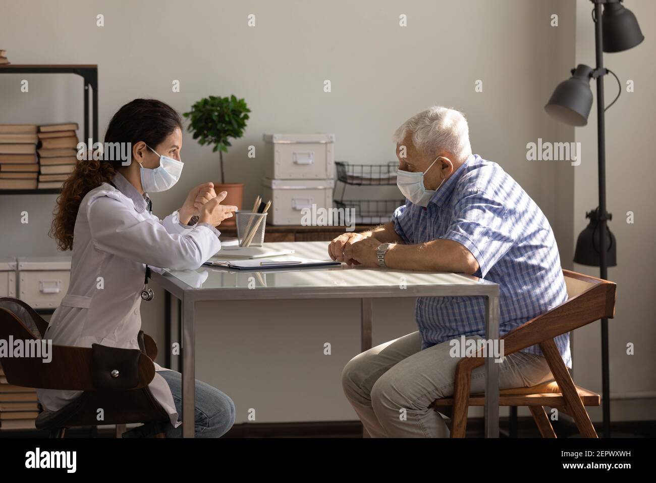 Vue latérale femme médecin portant un masque facial consultant homme âgé Banque D'Images