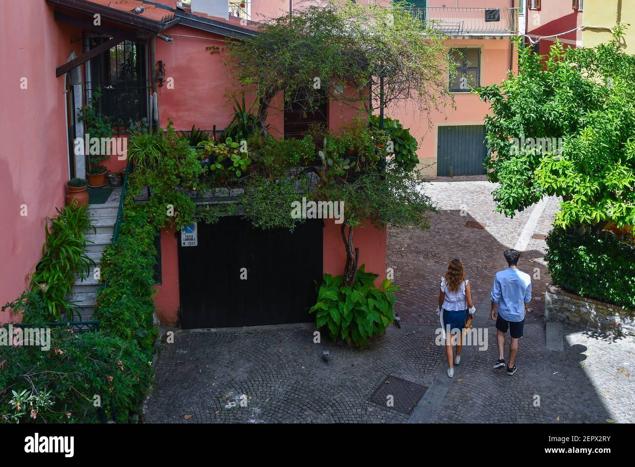 Un jeune couple marchant dans une ruelle de la vieille ville de Sarzana avec des plantes vertes parmi les maisons colorées typiques en été, la Spezia, Ligurie, Italie Banque D'Images