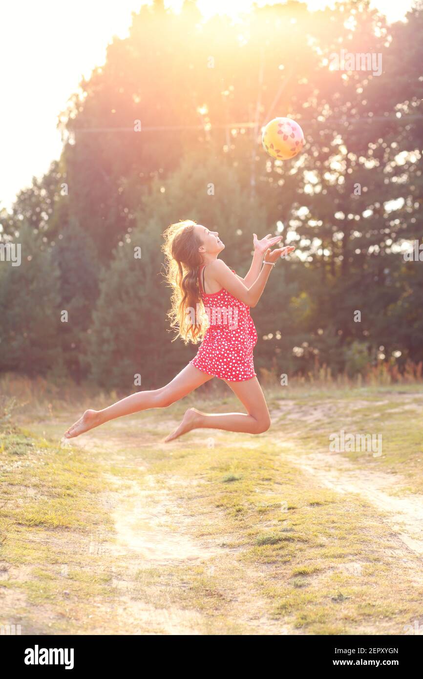 Portrait de la belle adolescente fille saute et joue avec le ballon au coucher du soleil d'été. Mise au point douce Banque D'Images