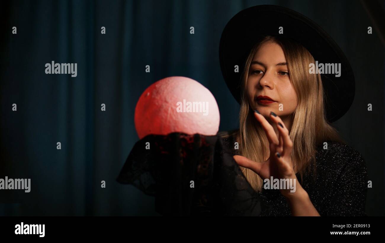 Une jeune femme qui tient une balle magique tient dans un chapeau. Belle femme psychique devine avec une boule magique rouge Banque D'Images