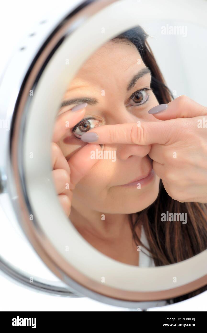 une femme de 50 ans à courte vue met une lentille de contact devant elle du miroir Banque D'Images