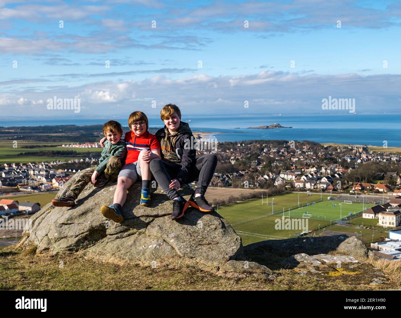 North Berwick, East Lothian, Écosse, Royaume-Uni, 28 février 2021.Escalade de la loi de Berwick pour le syndrome de Rett : le jour des maladies rares, Nina McKinney, âgée de 7 ans, grimpe la colline de 613 pieds chaque jour ce mois-ci pour recueillir de l'argent pour Reverse Rett, un organisme de bienfaisance qui soutient la recherche sur le trouble dont souffre sa sœur.Nina a bravé tout le temps et heureusement le soleil d'aujourd'hui.Photo: Nina avec ses deux frères Angus, 11 ans et Felix, 4 ans s'assoient sur un rocher surplombant North Berwick Banque D'Images