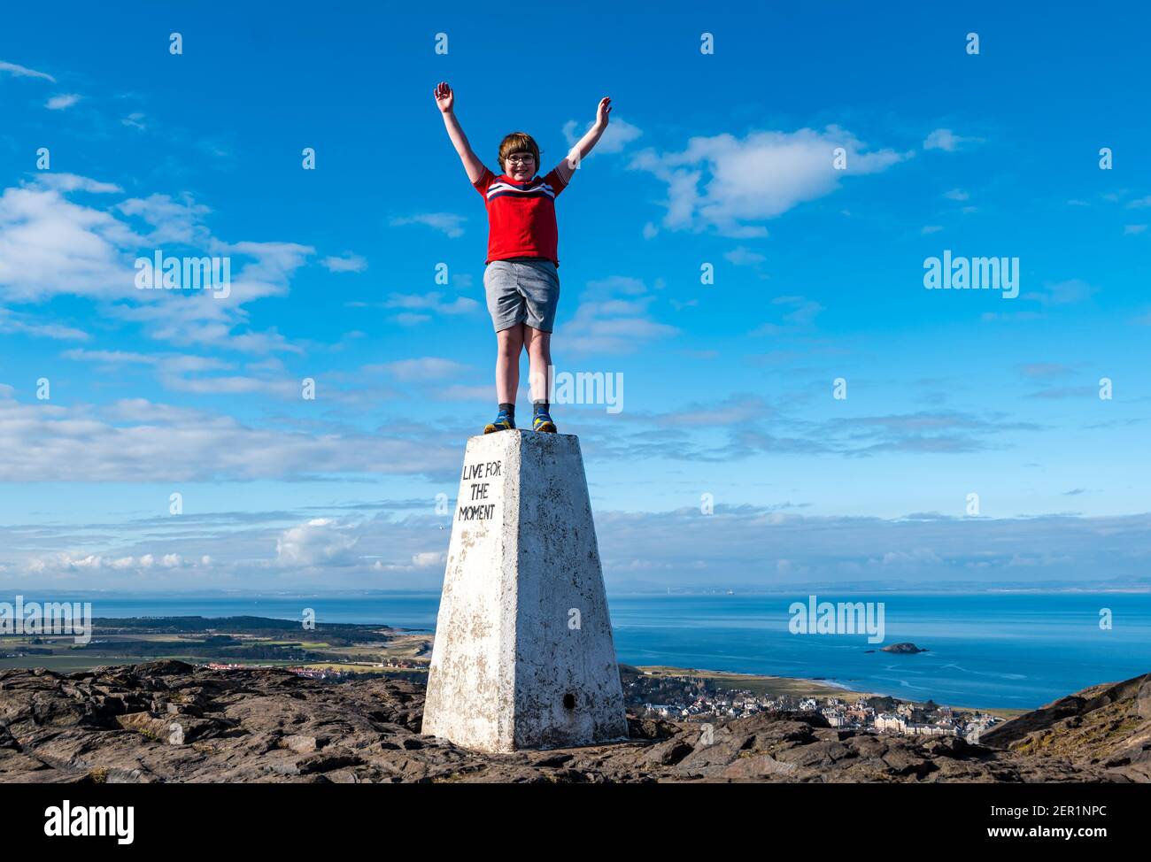 North Berwick, East Lothian, Écosse, Royaume-Uni, 28 février 2021.Escalade de la loi de Berwick pour le syndrome de Rett : le jour des maladies rares, Nina McKinney, âgée de 7 ans, termine son objectif de gravir la colline de 613 pieds chaque jour ce mois-ci pour recueillir de l'argent pour l'organisme de bienfaisance Reverse Rett, qui soutient la recherche sur le trouble dont sa sœur souffre.Nina célèbre la fin de sa campagne de collecte de fonds au sommet de la colline debout sur un point trigpoint avec le mot « Live for the moment » bravant tous les temps pendant le mois de février Banque D'Images