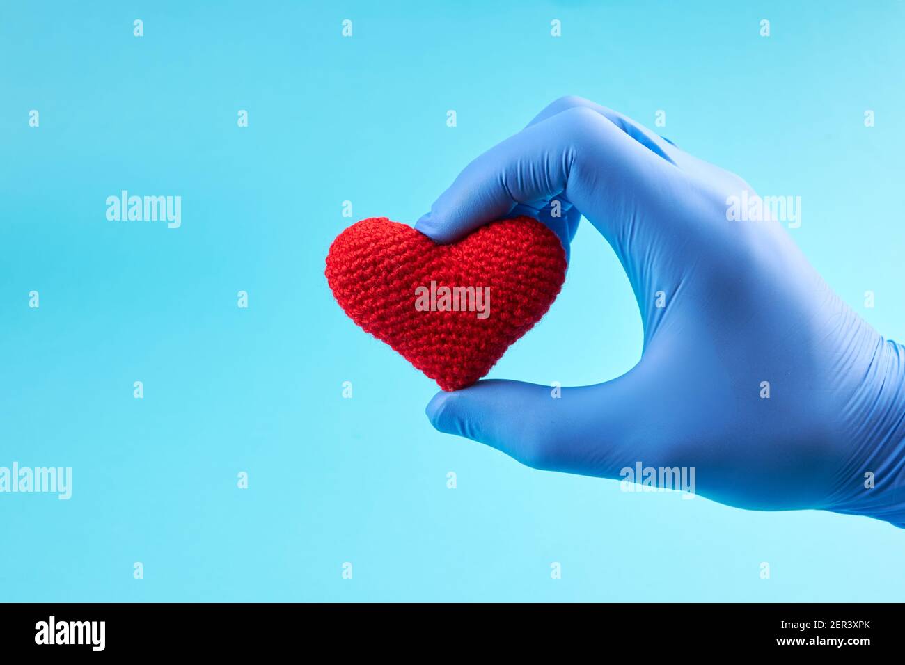 symbole coeur rouge à la main avec gants médicaux bleus. fond bleu clair avec espace de copie. concept de maladie cardiaque Banque D'Images