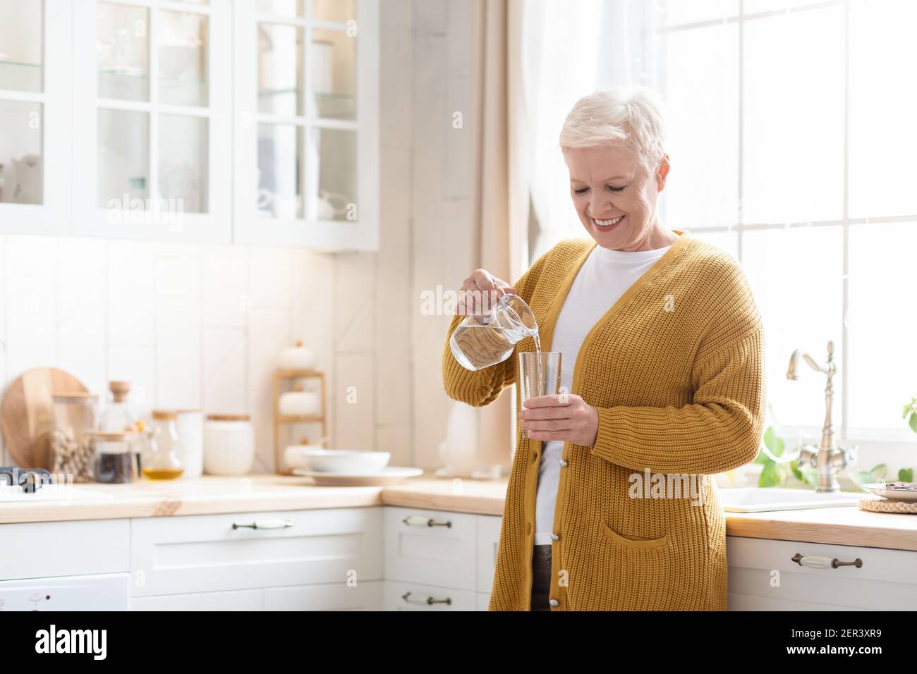 Bonne femme âgée qui verse de l'eau dans le verre de la cuisine Banque D'Images