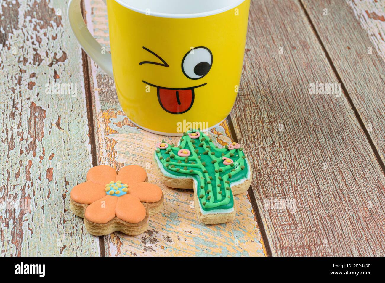 Biscuits de fleurs et de cactus, à côté d'une tasse jaune montrant la langue. Banque D'Images