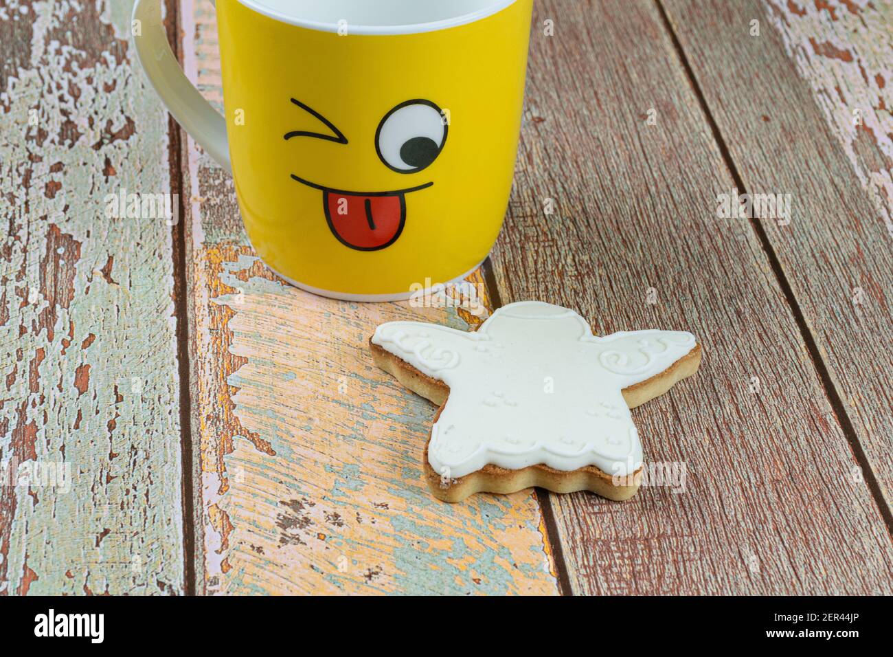 Biscuit en forme d'ange sur une table en bois, à côté d'une tasse jaune montrant la langue. Banque D'Images