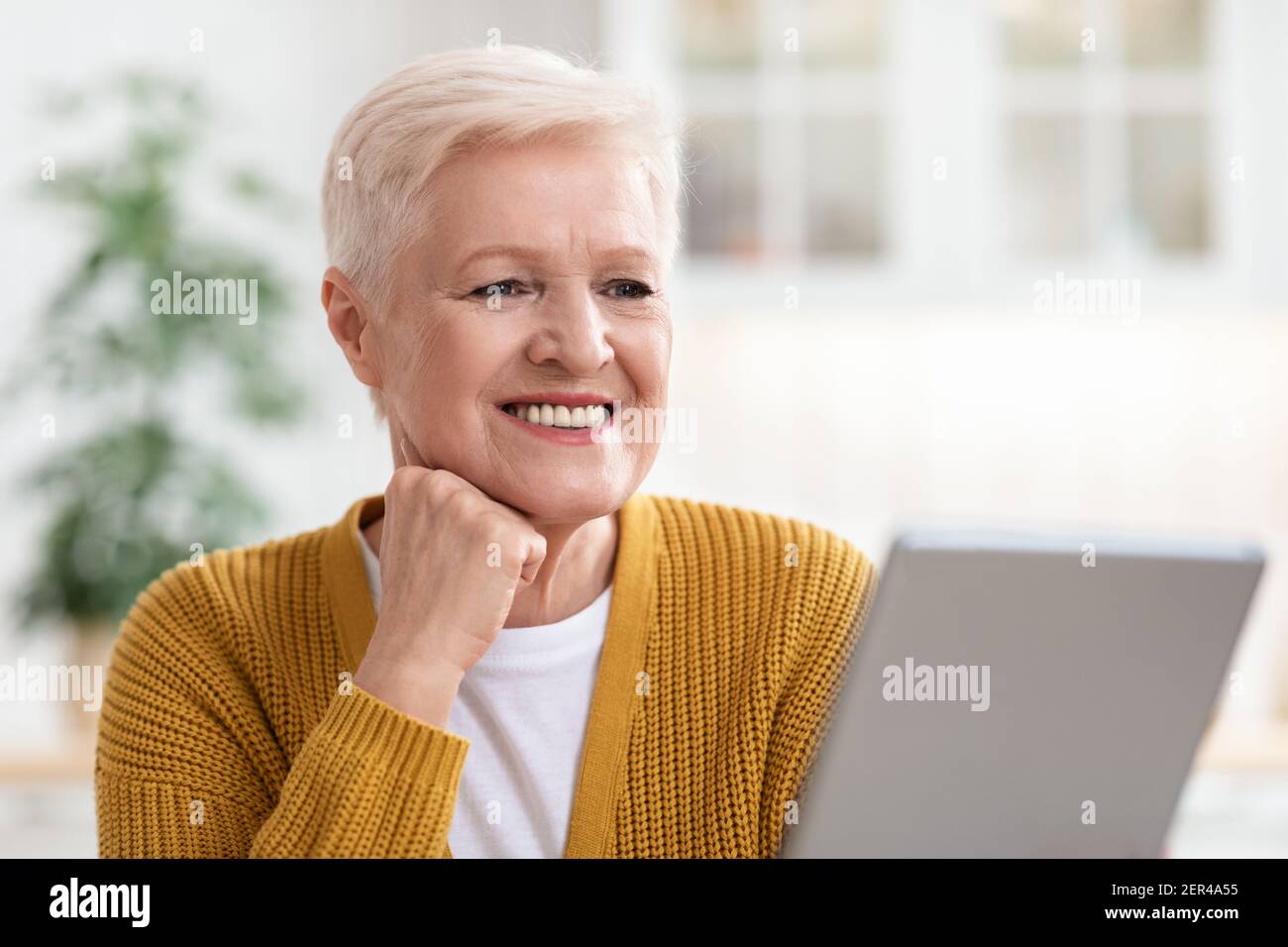 Bonne vieille femme utilisant une tablette numérique dans la cuisine Banque D'Images