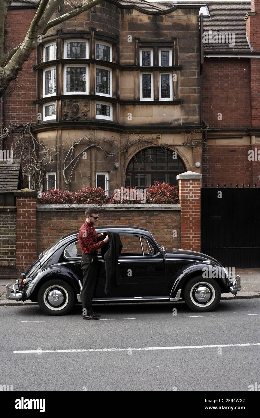 Jeune homme sortant de la voiture vintage noir volkswagen scarabée Banque D'Images