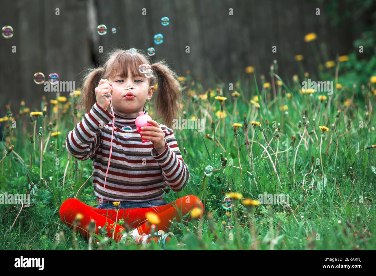 Drôle belle petite fille soufflant des bulles de savon dans le parc. Banque D'Images