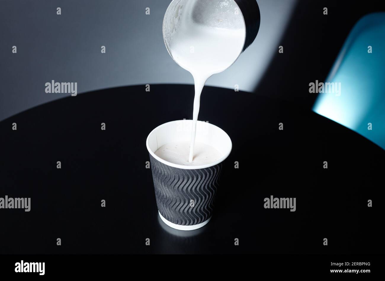 Le barista verse du lait dans une tasse en papier jetable sur une table en bois dans un café. Préparer une boisson savoureuse au lait. Une femme tient le pichet de lait en métal à la main Banque D'Images