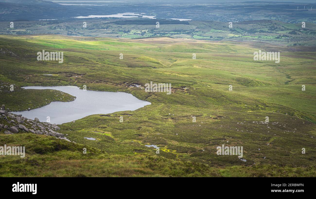 Vue depuis la montagne Cuilcagh sur les lacs, les prairies verdoyantes et les champs avec des taches de lumière du soleil dans la vallée ci-dessous, Irlande du Nord Banque D'Images