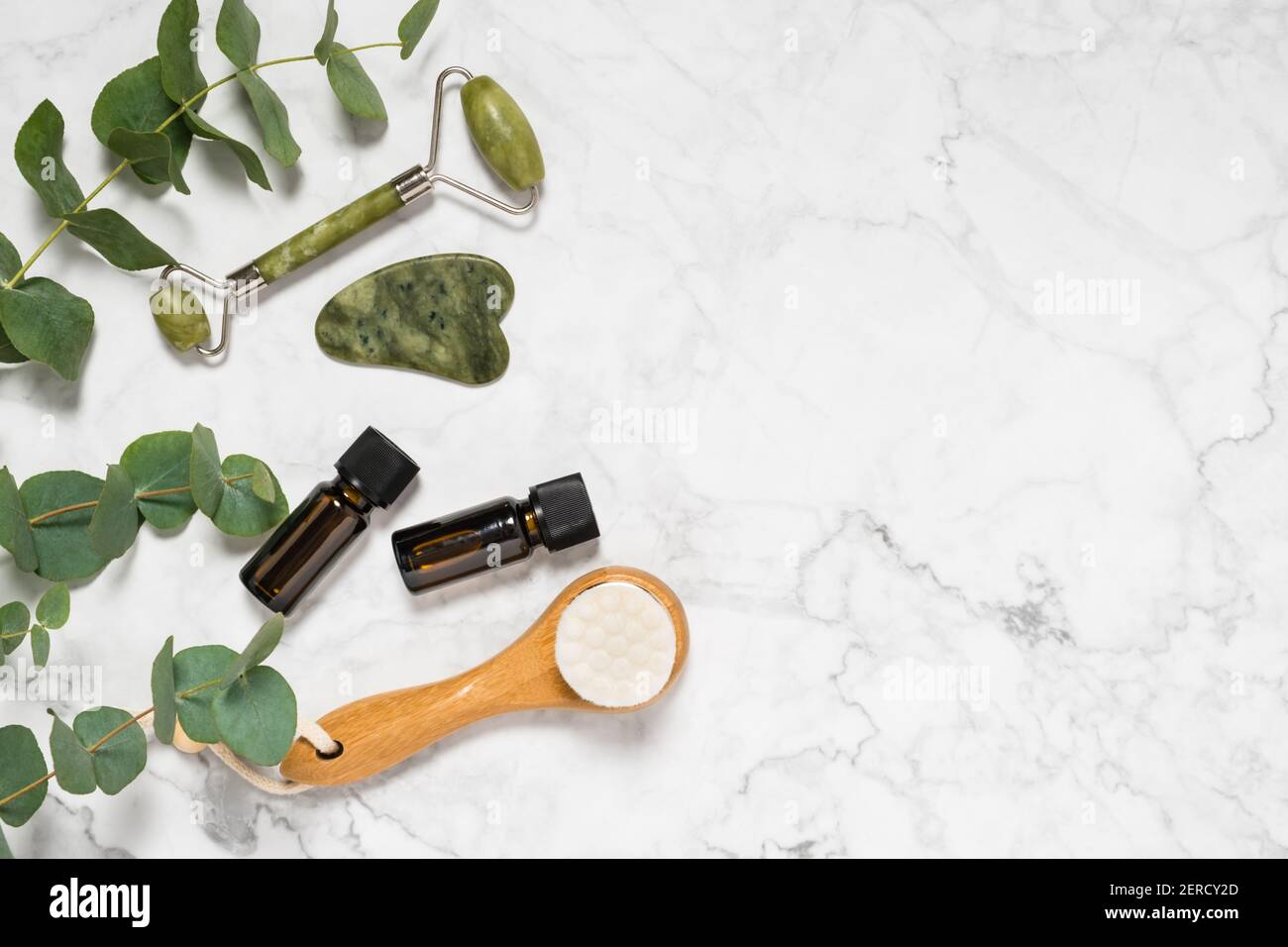 Soin naturel de la peau, spa et outils de bien-être: Rouleau de jade beauté,  pierre de gua sha, huile essentielle et brosse de visage en bois avec  branche d'eucalyptus sur bac de