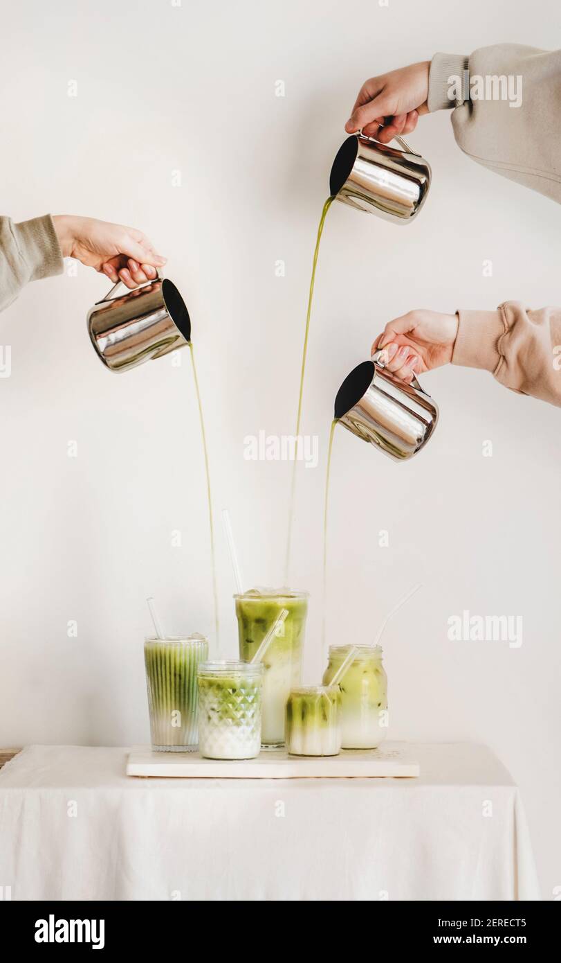 Mains de femmes versant le thé japonais matcha dans des verres avec du lait et faisant latte vert matcha pour le petit déjeuner à bord sur fond de mur léger. Café Banque D'Images