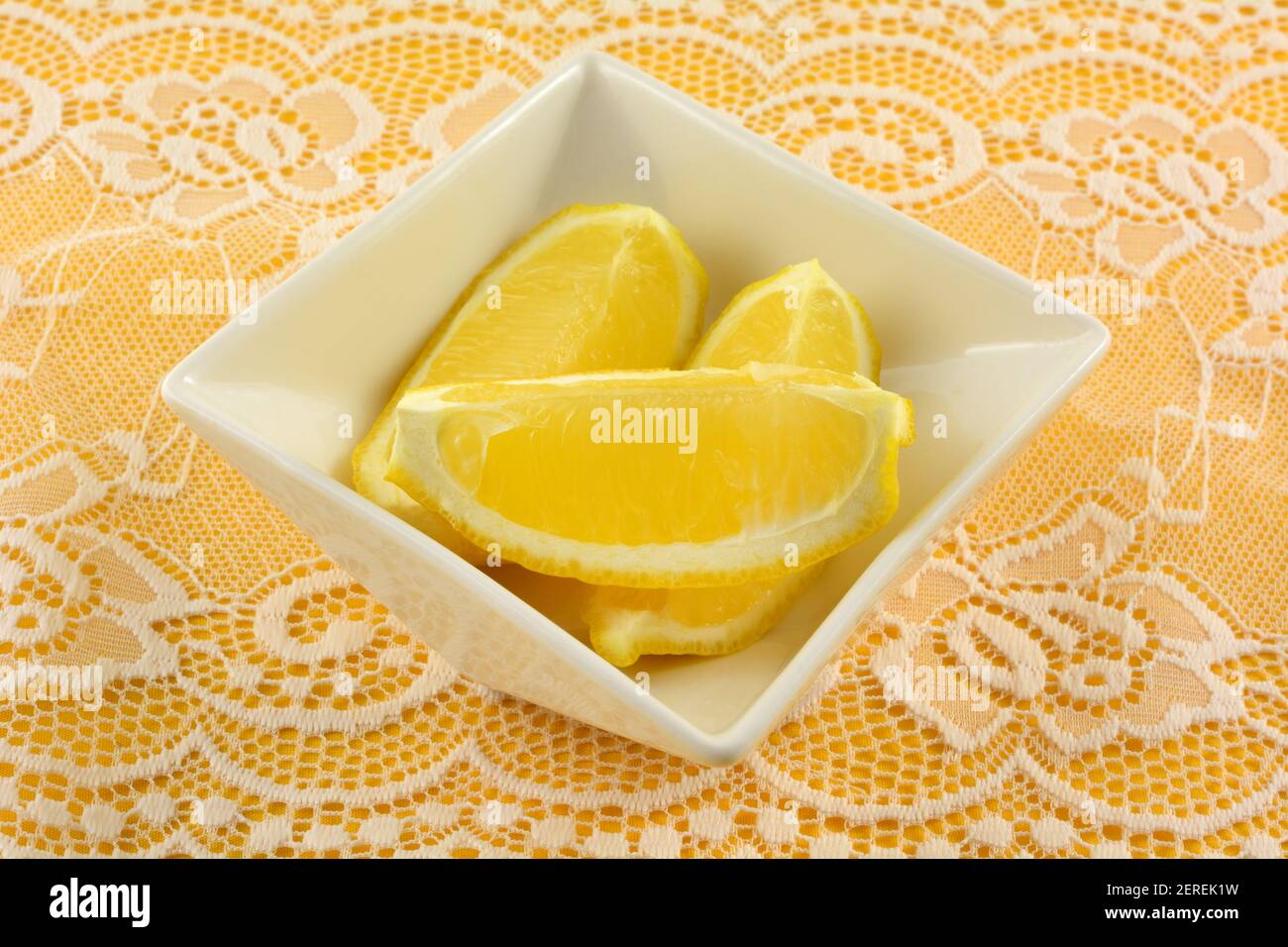 Tranches de citron frais dans un bol à ingrédients blancs sur du blanc dentelle sur nappe jaune Banque D'Images
