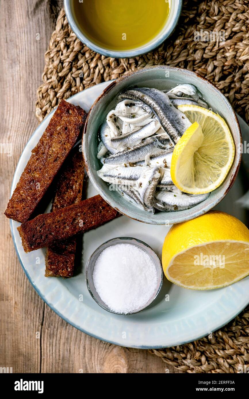 Bol d'anchois marinés ou filet de sardines dans l'huile, servi avec du citron, de l'huile d'olive, du sel et du pain de seigle grillé pour des tapas ou des antipasti sur le vieux bois b Banque D'Images