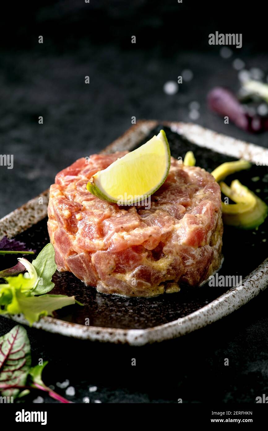 Tartare de thon avec salade verte, citron vert, avocat et sauce moutarde sur une plaque en céramique noire de style japonais sur fond de marbre noir. Restaurant Banque D'Images