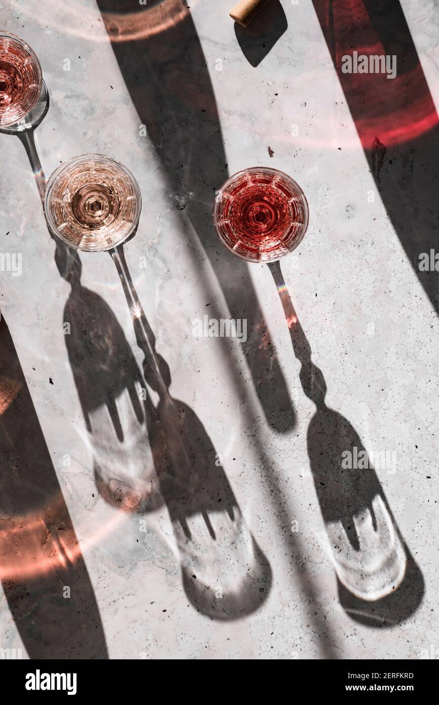 Trois nuances de vin de Rose dans des verres jetant des ombres dures entourées d'ombres colorées projetées à partir des bouteilles de vin. Banque D'Images