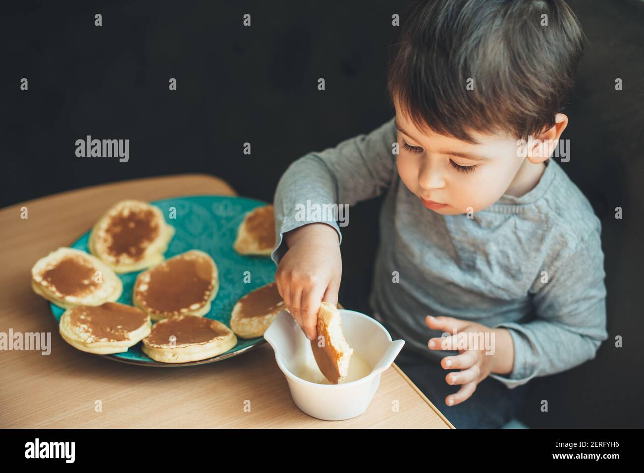 Un garçon caucasien affamé mangeant des crêpes seul à la table après jouer à la maison Banque D'Images