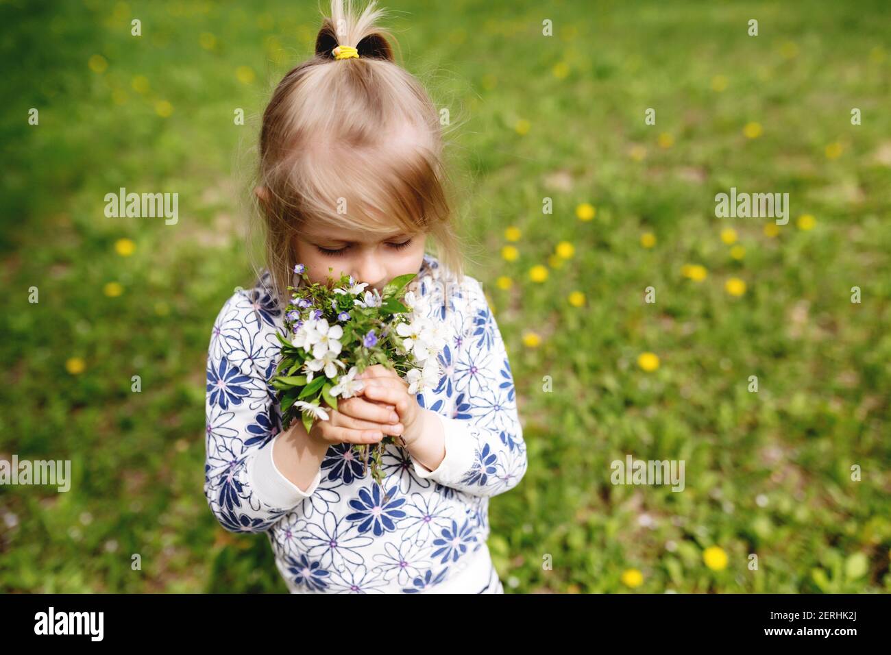 Une petite fille renifle des fleurs de printemps sur une pelouse verte dans le jardin. Photo de haute qualité Banque D'Images