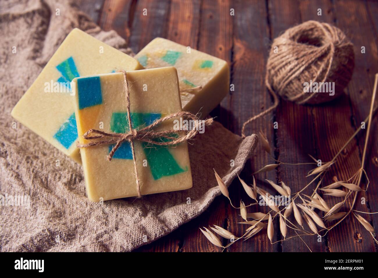 Un savon biologique parfumé fait main avec un motif géométrique, une serviette en lin et quelques épillets secs sur un comptoir en bois brun. Banque D'Images