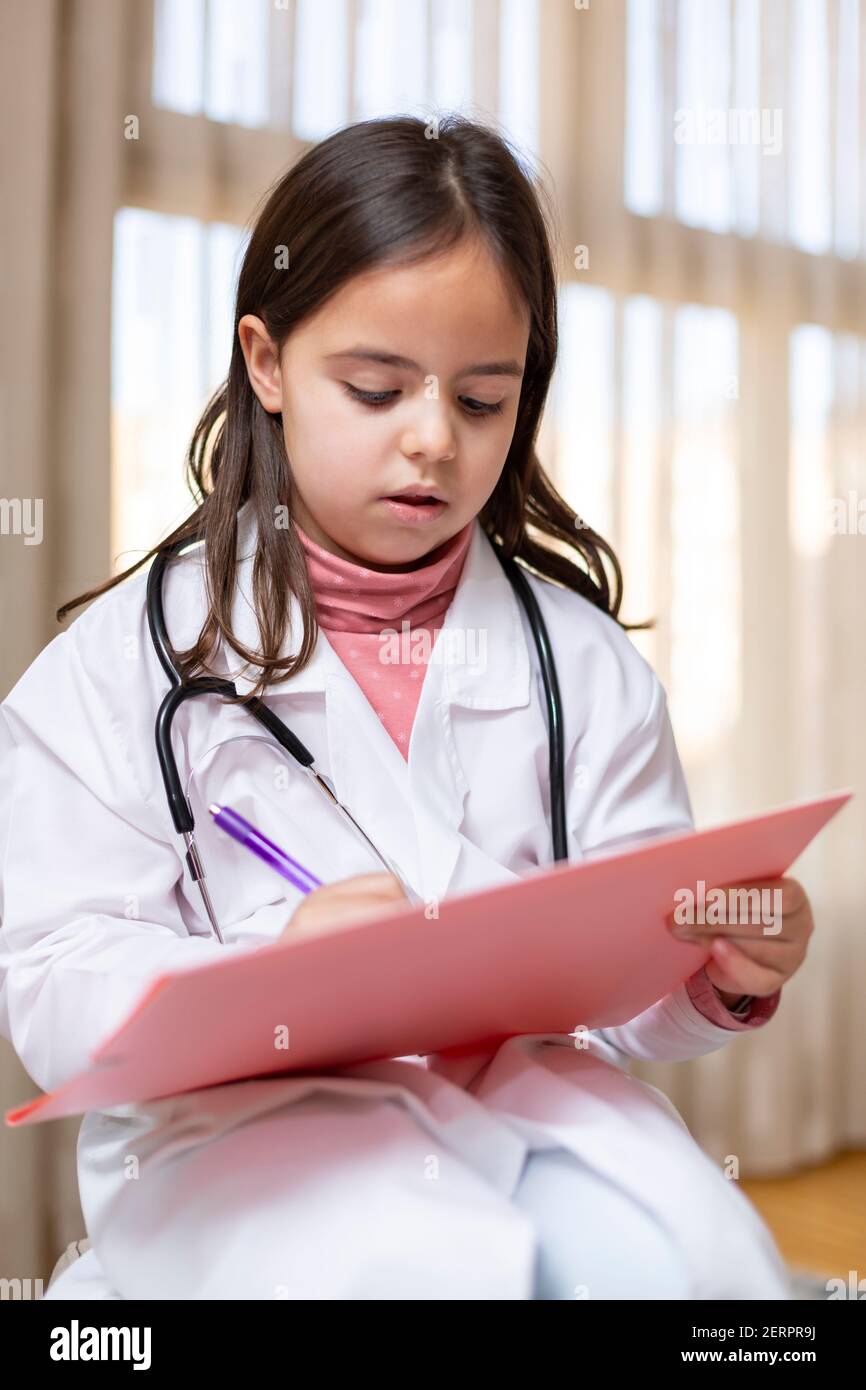 Portrait d'un petit enfant habillé comme une infirmière écrivant concentré dans un carnet. Elle joue à être médecin. Banque D'Images