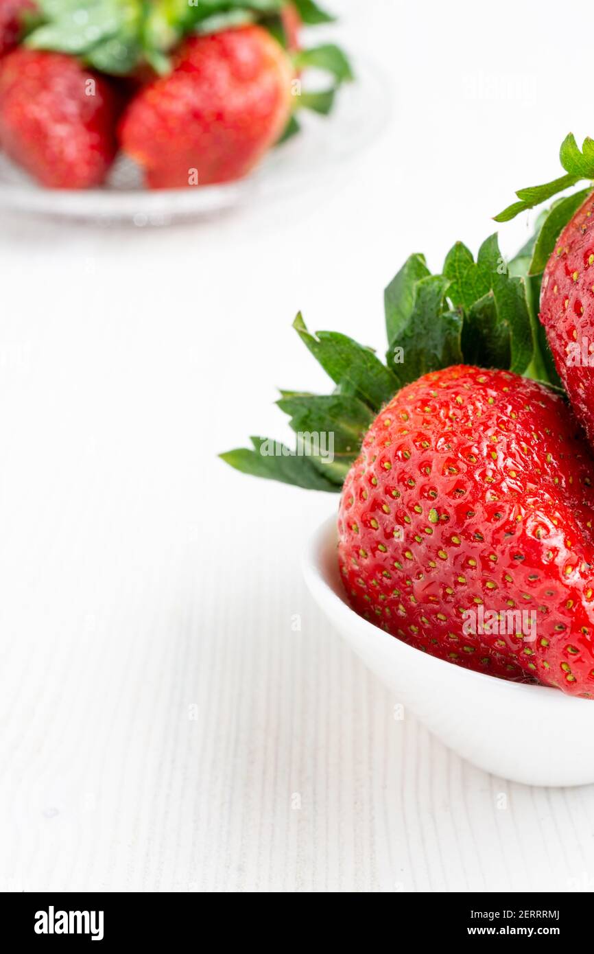 Vue de dessus des fraises dans un bol blanc et assiette avec plus de fraises, mise au point sélective, sur table blanche, à la verticale Banque D'Images